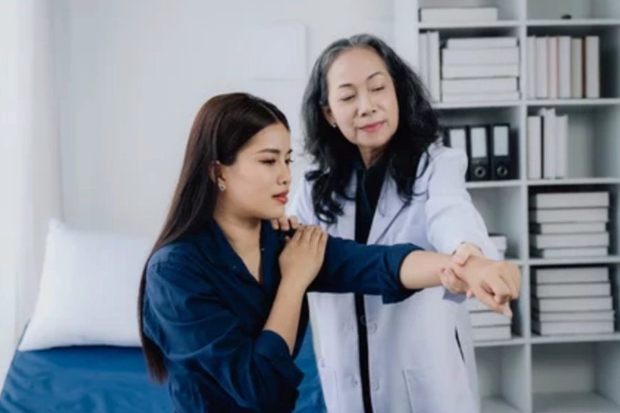 A clinician assessing shoulder movement and strength during a physical examination.