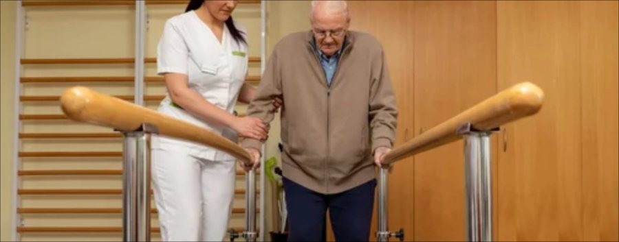 A therapist supporting a stroke survivor during walking practice in a rehabilitation gym.