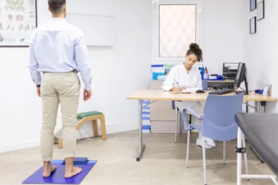 A person standing on a balance pad during a clinical balance assessment, with a clinician recording the result.